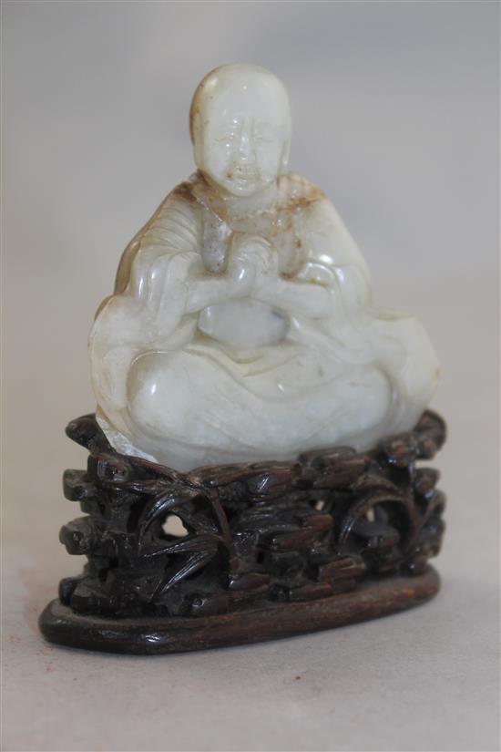 A Chinese white and russet jade carving of a luohan, 18th / 19th century, 6.7cm, neck broken and restuck, intricately carved rosewood s